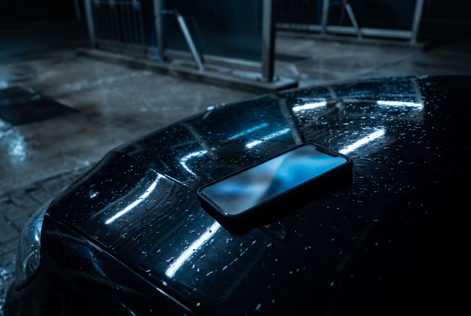 Celular sobre o capô molhado de um carro preto, com a tela acesa e luz azul